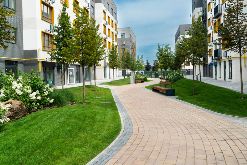 Courtyard walkway between two multi-story buildings with yellow window trim. Green grass with flow gardens and many trees.