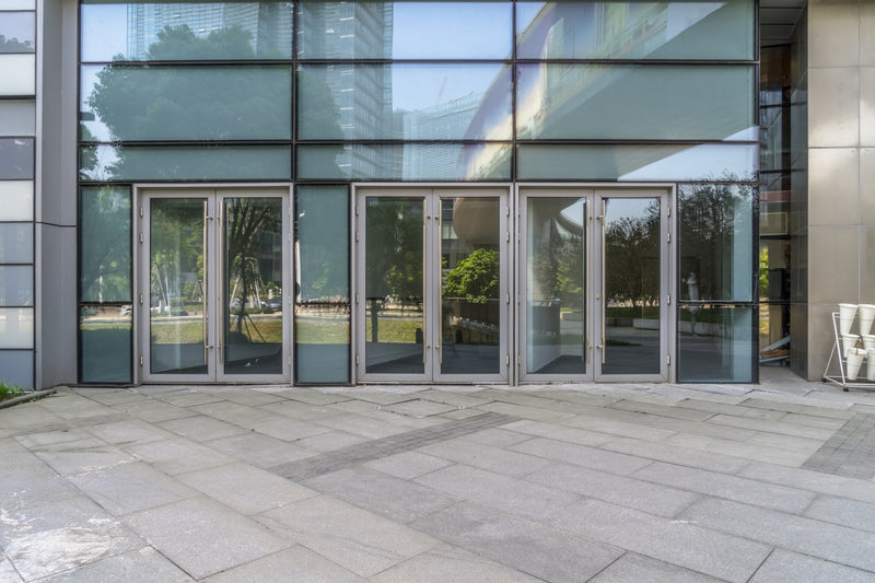 Commercial entrance with tall glass windows and multiple metal doors.