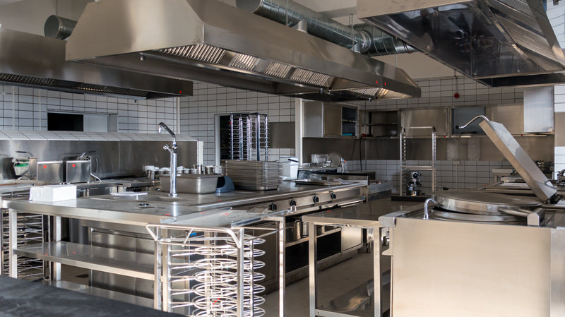 Stainless steel commercial kitchen with range hoods and exhaust vents. 