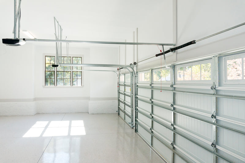 Interior of a white garage with two large roll up doors and garage door opener mechanisms. 