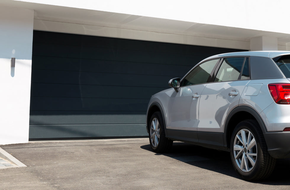 A silver compact SUV parked in front of a modern white home with a large dark garage door.
