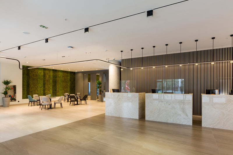 Lobby area with multiple marble reception desks, a slatted wood accent wall, and a green living wall in the background.