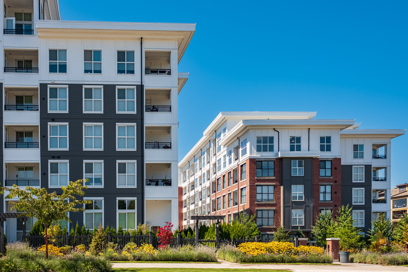 Two low-rise condo buildings with landscaped greenery in front and a clear blue sky above.