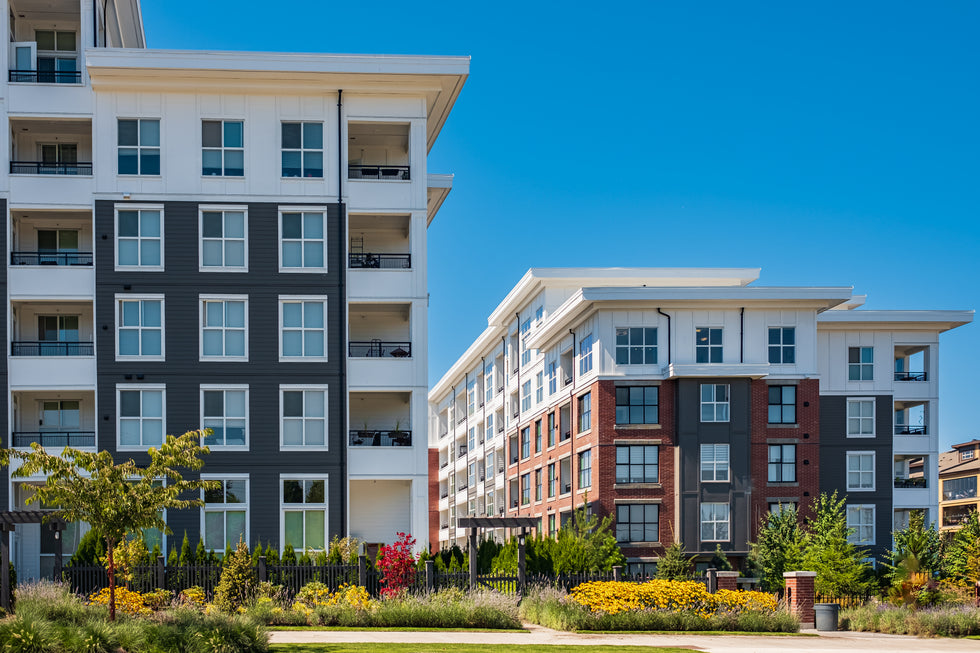 Two low-rise condo buildings with landscaped greenery in front and a clear blue sky above.