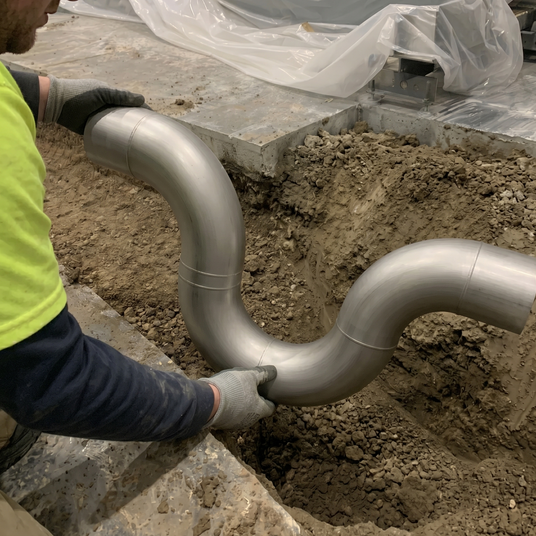 stainless steel running trap held by plumbing installer inside trench