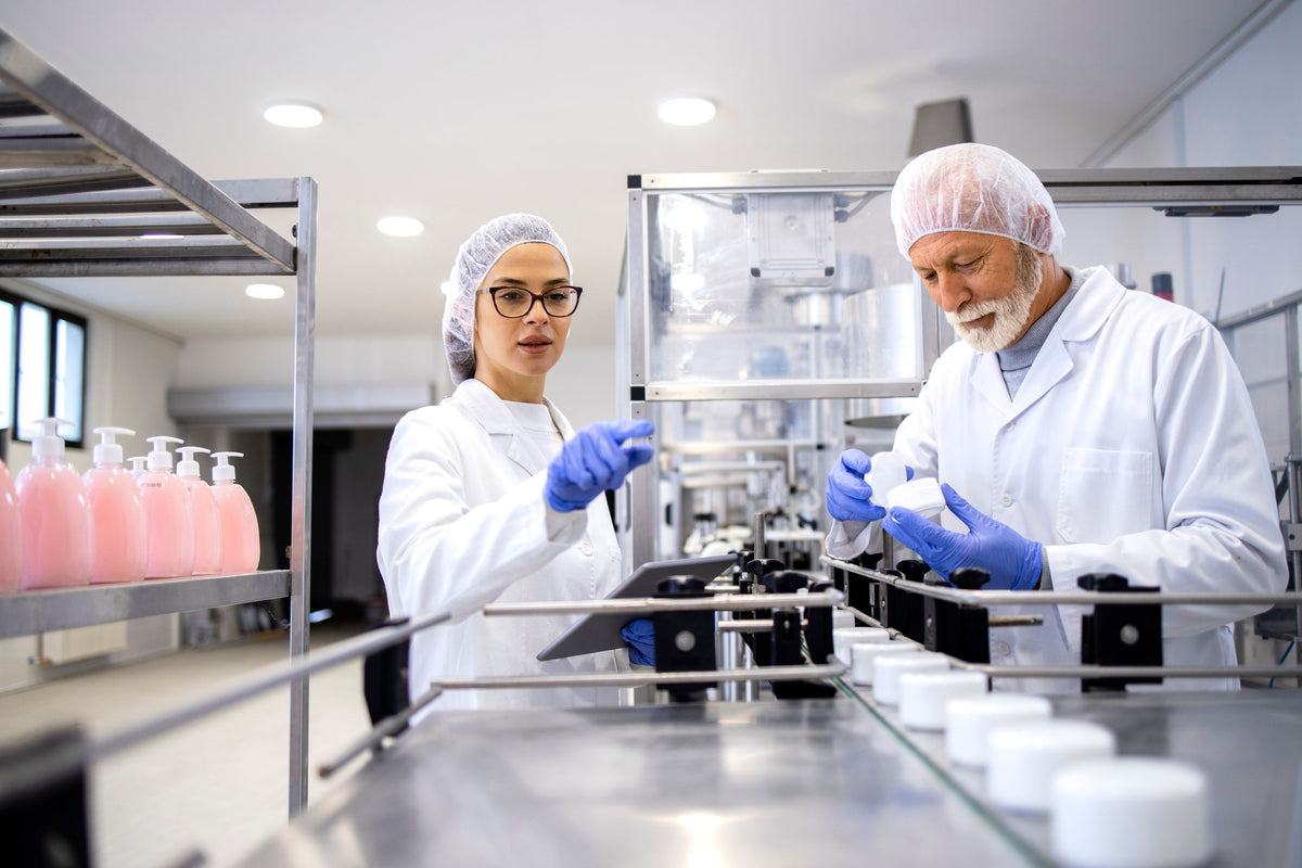 Two workers in lab coats inspecting product from cosmetic lab
