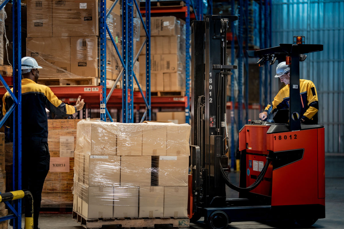 man operating forklift while other worker guides him through aisle inside warehouse