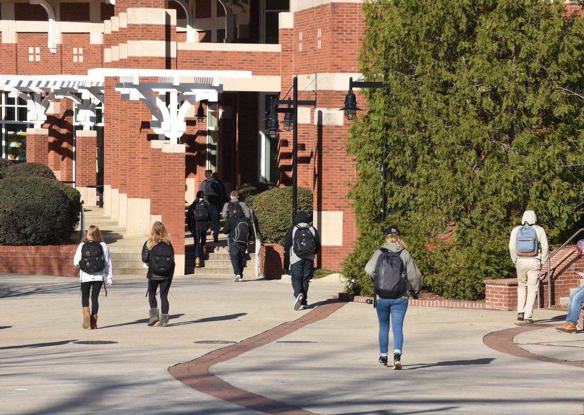 Students walking on a college campus with brick buildings and greenery.